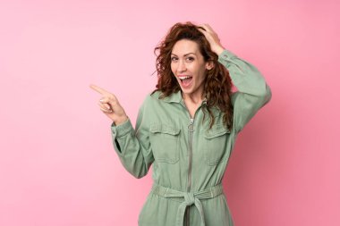 Soyutlanmış pembe arka planda genç ve güzel bir kadın. Şaşırmış ve işaret ediyor.