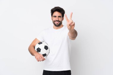 Sakallı yakışıklı genç adam izole beyaz arka planda gülümsüyor ve zafer işareti gösteriyor.