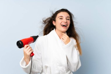 Saç kurutma makineli bornozlu genç bir kadın.