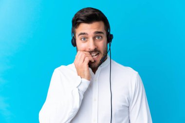Tele pazarlamacı, mavi arka plan üzerinde bir kulaklıkla çalışıyor. Gergin ve korkmuş.