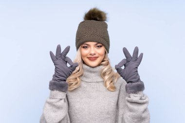 Kışlık şapkalı genç kız izole edilmiş mavi arka planda parmaklarıyla 