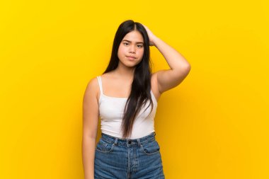 Asyalı genç bir kız, izole edilmiş sarı arka planda, hayal kırıklığı ifadesi var ve anlamıyor.