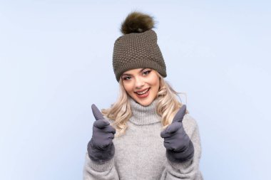 Kışlık şapkalı genç kız izole edilmiş mavi arka planda seni işaret ediyor.