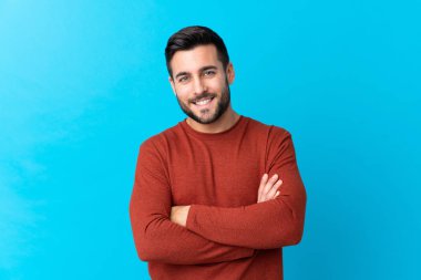 Sakallı, genç ve yakışıklı bir adam mavi arka planda gülüyor.