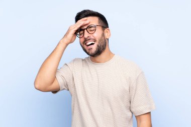 Sakallı, genç ve yakışıklı bir adam mavi arka planda gülüyor.