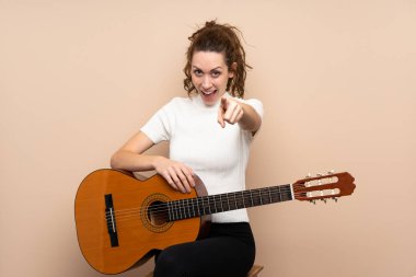 Arka planda gitar çalan genç bir kadın şaşırmış ve ön tarafı işaret ediyor.