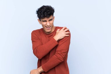 Arjantinli genç bir adam izole edilmiş mavi arka planda çabaladığı için omuz ağrısı çekiyor.