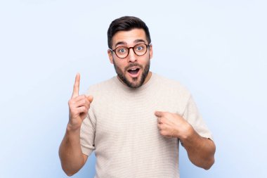 Sakallı, mavi arka planda, yüzünde sürpriz bir ifade olan yakışıklı bir genç.