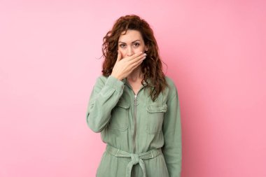 İzole edilmiş pembe arka planı olan genç ve güzel bir kadın elleriyle ağzını kapatıyor.