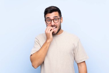 Sakallı, genç ve yakışıklı bir adam mavi arka planda gergin ve korkmuş.