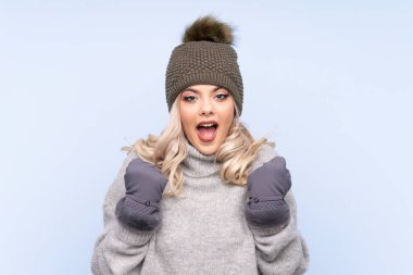 Kışlık şapkalı genç kız izole edilmiş mavi arka planda zaferi kutluyor.