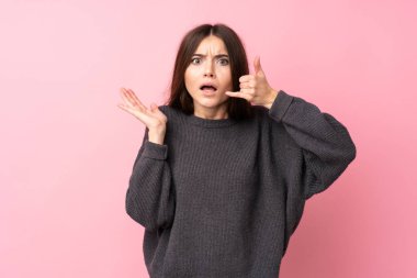 Soyutlanmış pembe arka planı olan genç bir kadın telefon jesti yapıyor.