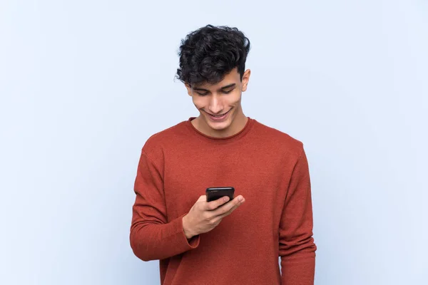 Joven Argentino Sobre Fondo Azul Aislado Enviando Mensaje Con Móvil —  Fotos de Stock