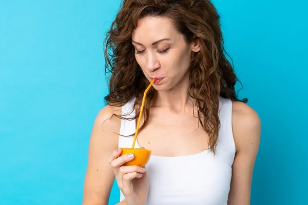 Ung kvinna med lockigt hår håller en orange över isolerad blå bakgrund — Stockfoto