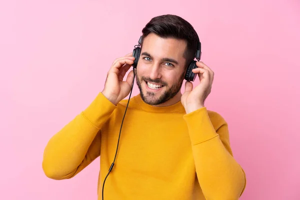 Молодой красивый мужчина с бородой слушает музыку над изолированным розовым — стоковое фото