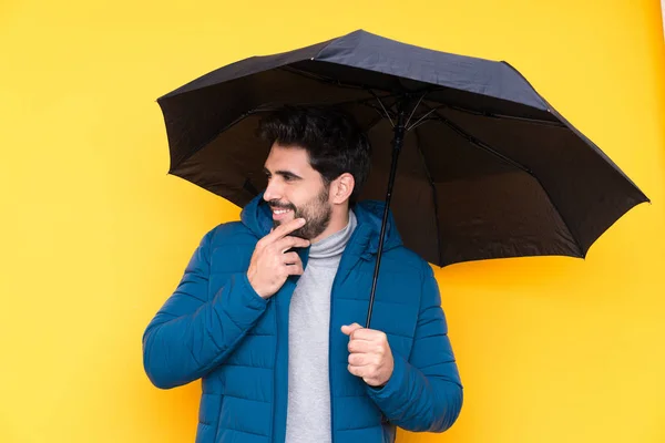 孤立した黄色の背景の上に傘を持っている男は考えと側を見て — ストック写真