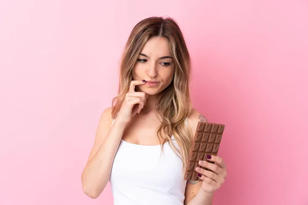 분홍색 배경을 여자가 초콜릿 알약을 먹으면서 의심을 — 스톡 사진