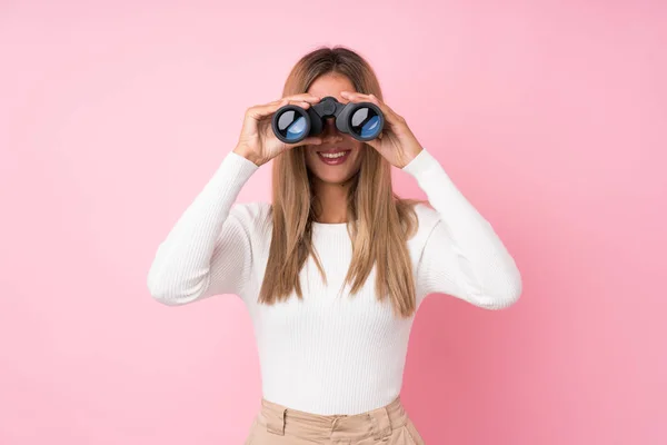 Mujer Rubia Joven Sobre Fondo Rosa Aislado Con Binoculares Negros —  Fotos de Stock