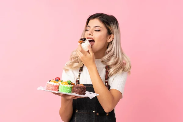 Tiener Meisje Geïsoleerde Roze Achtergrond Holding Mini Cakes Eten Het — Stockfoto