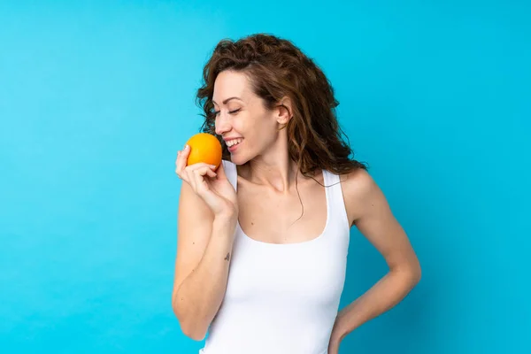 Ung kvinna med lockigt hår håller en orange över isolerad blå bakgrund — Stockfoto