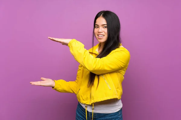 年轻的少年亚洲女孩在孤立的紫色背景上拿着复制空间插入广告 — 图库照片