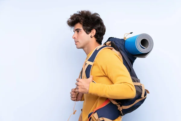 Jovem montanhista homem com uma grande mochila sobre bac azul isolado — Fotografia de Stock