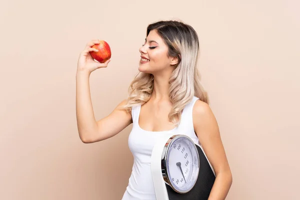 Teenager girl with weighing machine over isolated background with weighing machine and with an apple