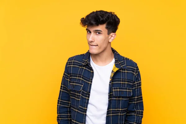 Young Argentinian man over isolated yellow background having doubts and with confuse face expression