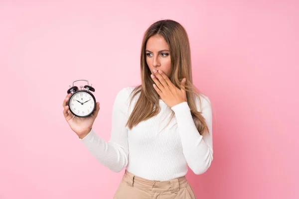 Joven Mujer Rubia Sobre Fondo Rosa Aislado Sosteniendo Reloj Despertador — Foto de Stock