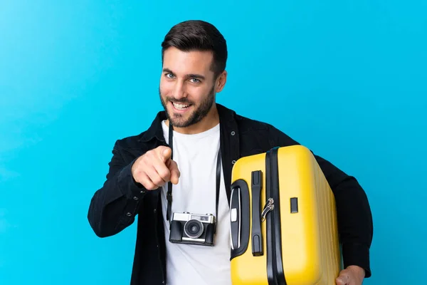 Cestovatel Muž Drží Kufr Přes Izolované Modré Pozadí Ukazuje Prstem — Stock fotografie