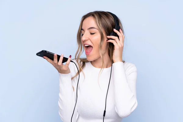 Mujer Joven Sobre Fondo Azul Aislado Escuchando Música Con Móvil —  Fotos de Stock