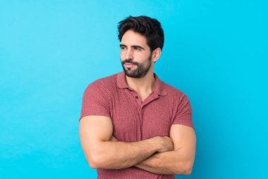 İzole edilmiş mavi arkaplan portresi üzerinde sakallı yakışıklı bir genç.