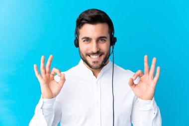 Tele pazarlamacı, mavi arka planda kulaklıkla çalışıyor. Parmaklarıyla 