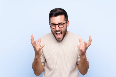 Sakallı, mavi arka planda genç ve yakışıklı bir adam mutsuz ve hayal kırıklığına uğramış.