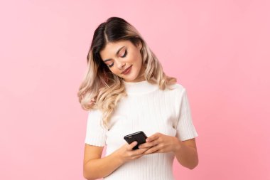 Pembe arka planda, kulaklıklı cep telefonunu kullanan genç bir kız.