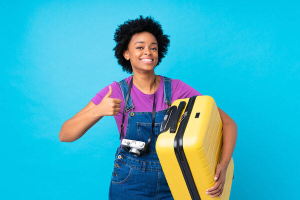 Африканская американка женщина путешественник с чемоданом на изолированном синем фоне с большим пальцем вверх, потому что что-то хорошее произошло
