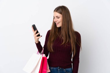 Elinde alışveriş poşetleri olan ve cep telefonuyla bir arkadaşına mesaj yazan izole edilmiş beyaz bir arka plan.