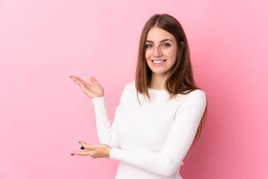Soyutlanmış pembe arka planda genç bir kadın. Davet edilmek için ellerini yana uzatıyor.