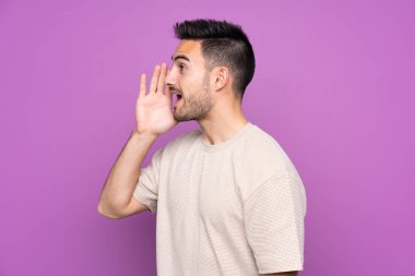 Young handsome man over isolated purple background shouting with mouth wide open to the lateral