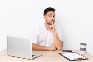 Young business man with a mobile phone in a workplace doing silence gesture