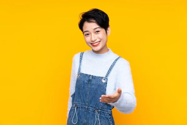 Young Asian Girl Overalls Isolated Yellow Background Handshaking Good Deal — 图库照片