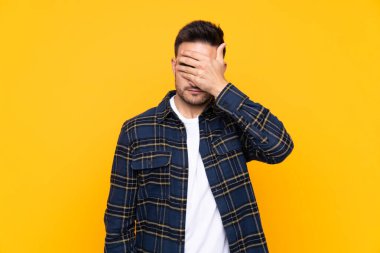 Elleri ile gözleri kaplayan izole sarı arka plan üzerinde genç yakışıklı adam
