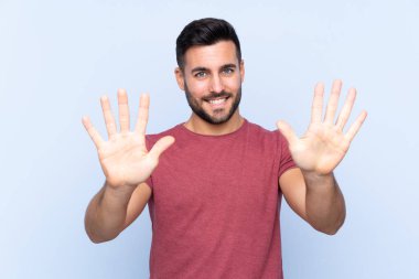 Sakallı, genç ve yakışıklı bir adam mavi arka planda parmaklarıyla ona kadar sayıyor.