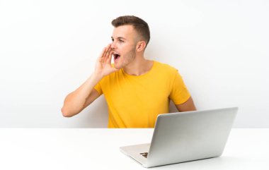 Masada dizüstü bilgisayarı olan genç sarışın adam ağzı açık bağırıyor.