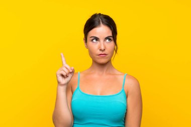 İşaret parmağı ile işaret izole sarı arka plan üzerinde genç kadın harika bir fikir