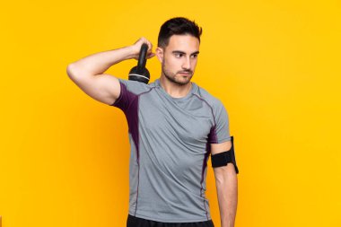 İzole edilmiş sarı duvardaki sporcu ağırlık kaldırıyor.