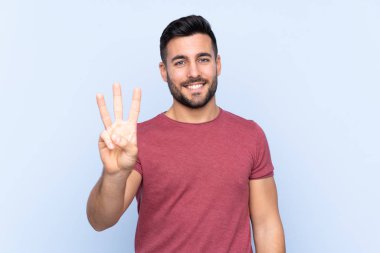 Mavi arka planda sakallı yakışıklı genç adam mutlu ve parmaklarıyla üçe kadar sayıyor.
