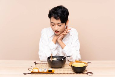 Genç Asyalı kız bir kase erişte ve suşiyle masada.