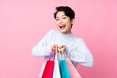 Soyutlanmış pembe arka planı olan genç Asyalı kız elinde alışveriş torbalarıyla şaşırdı.