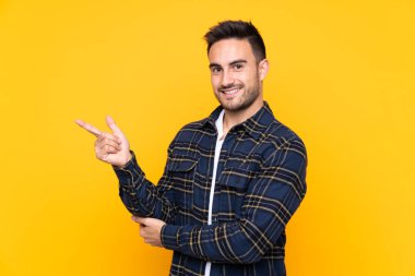 Izole sarı arka plan yan parmak işaret üzerinde Genç yakışıklı adam